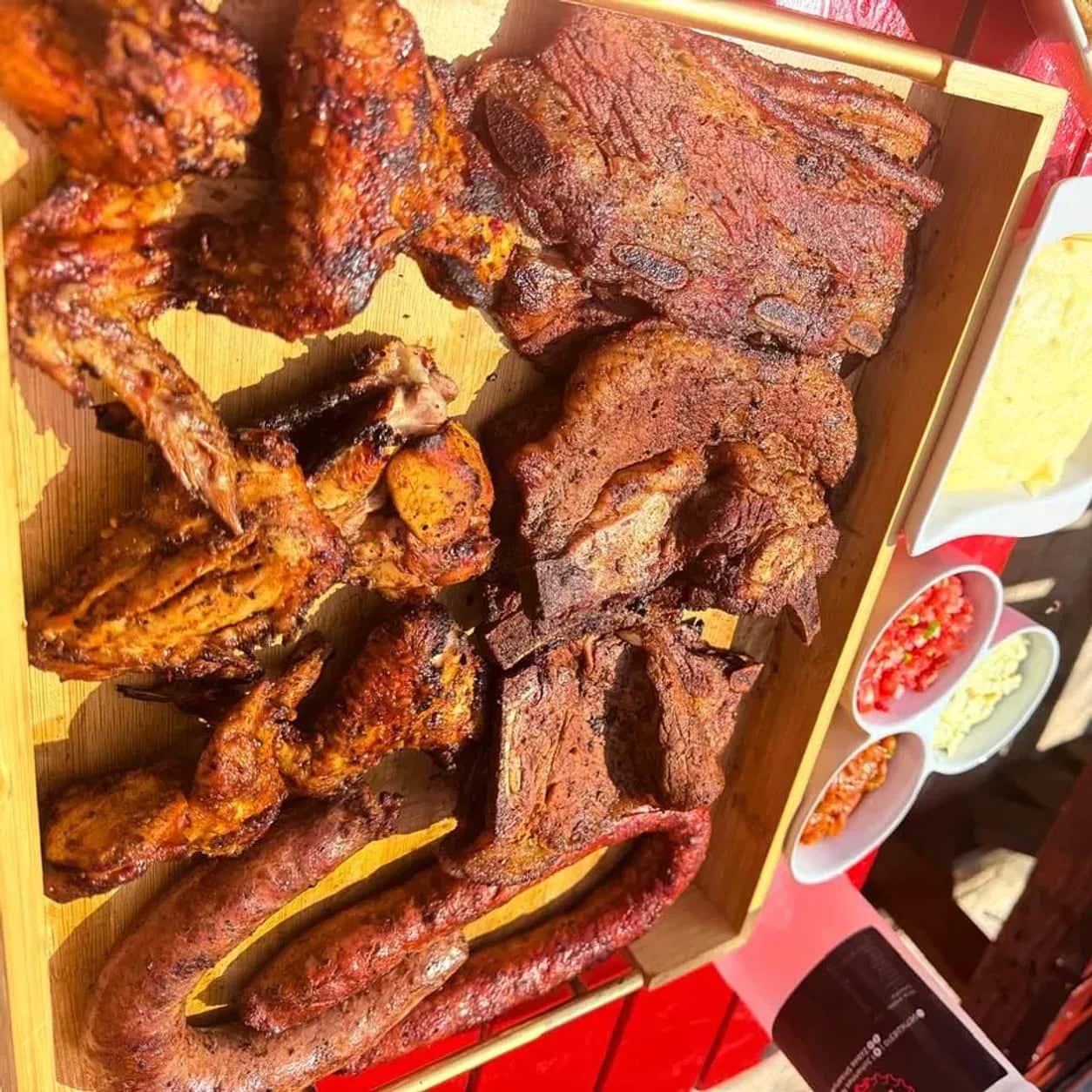 Flame-grilled chicken wings and beef ribs with pap and a tray of fresh salads on a wooden board