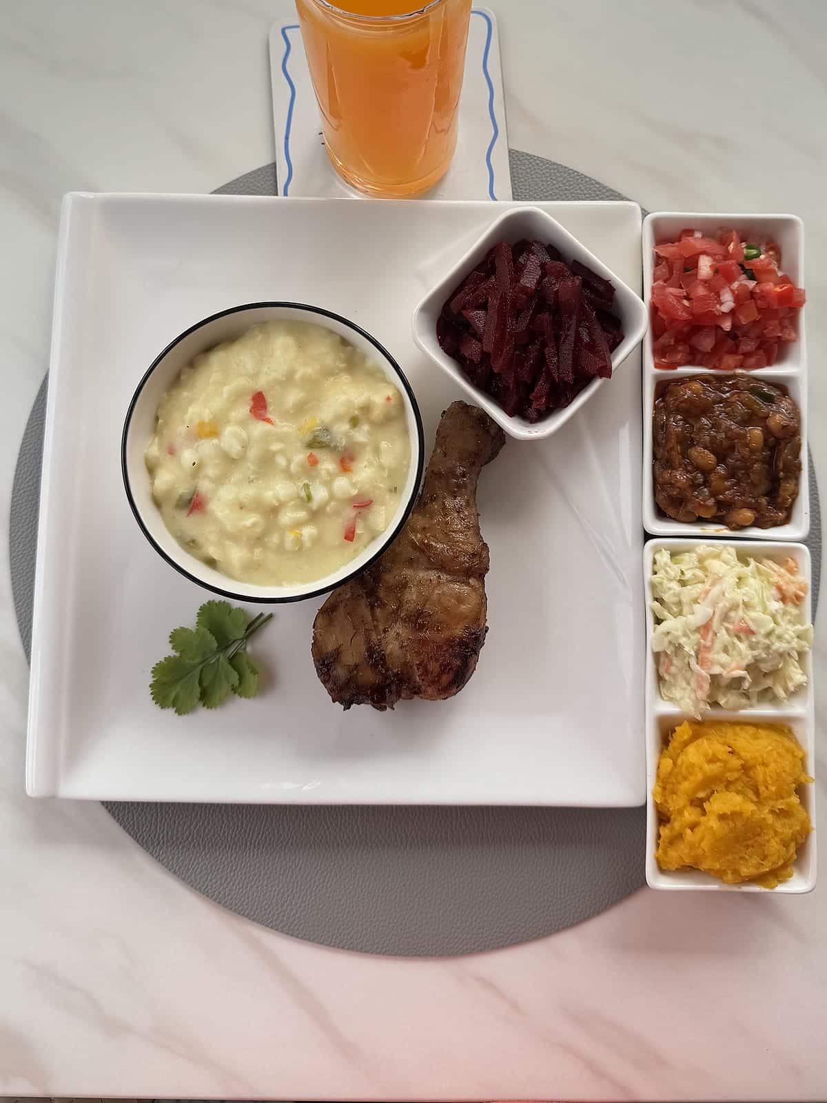A grilled chicken portion with creamy samp, beetroot and a tray of fresh sides