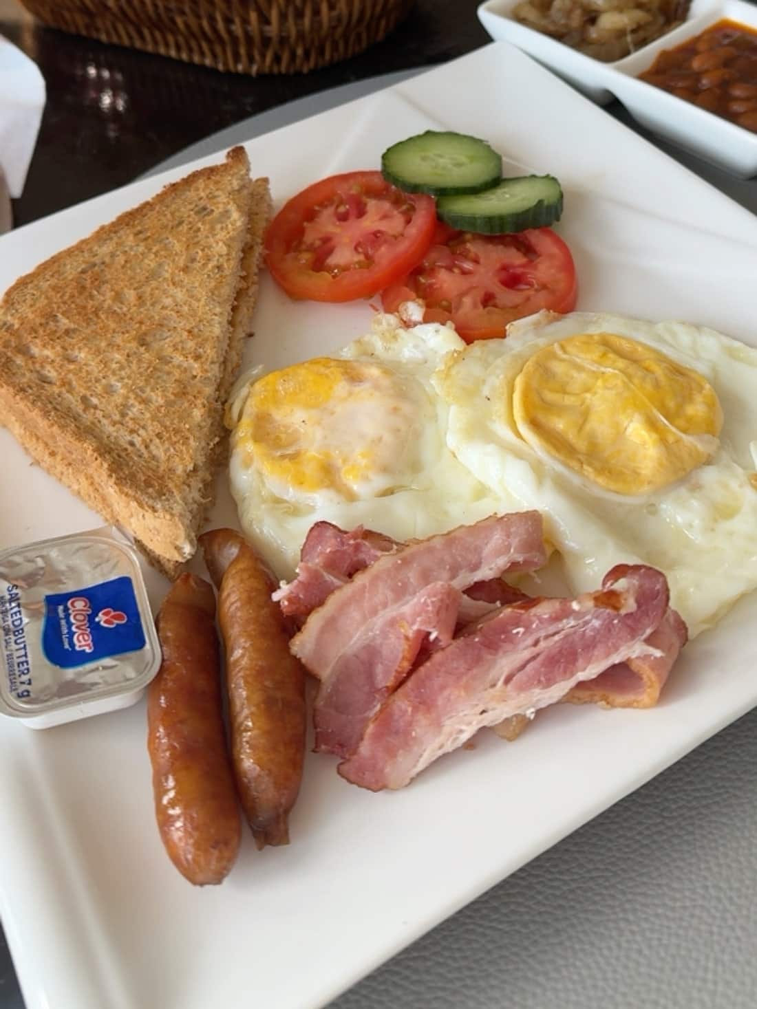 A full breakfast of eggs, bacon, sausage, toast and grilled tomato with beans and onions on the side
