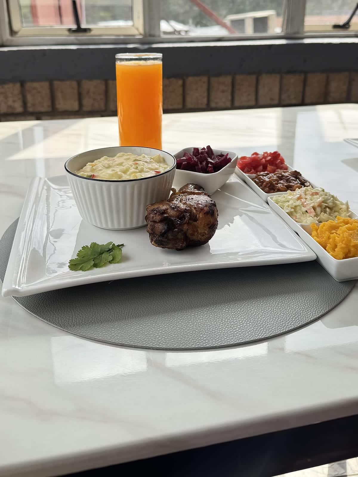 A plated chicken and samp meal with fresh juice by the window at Zaba's