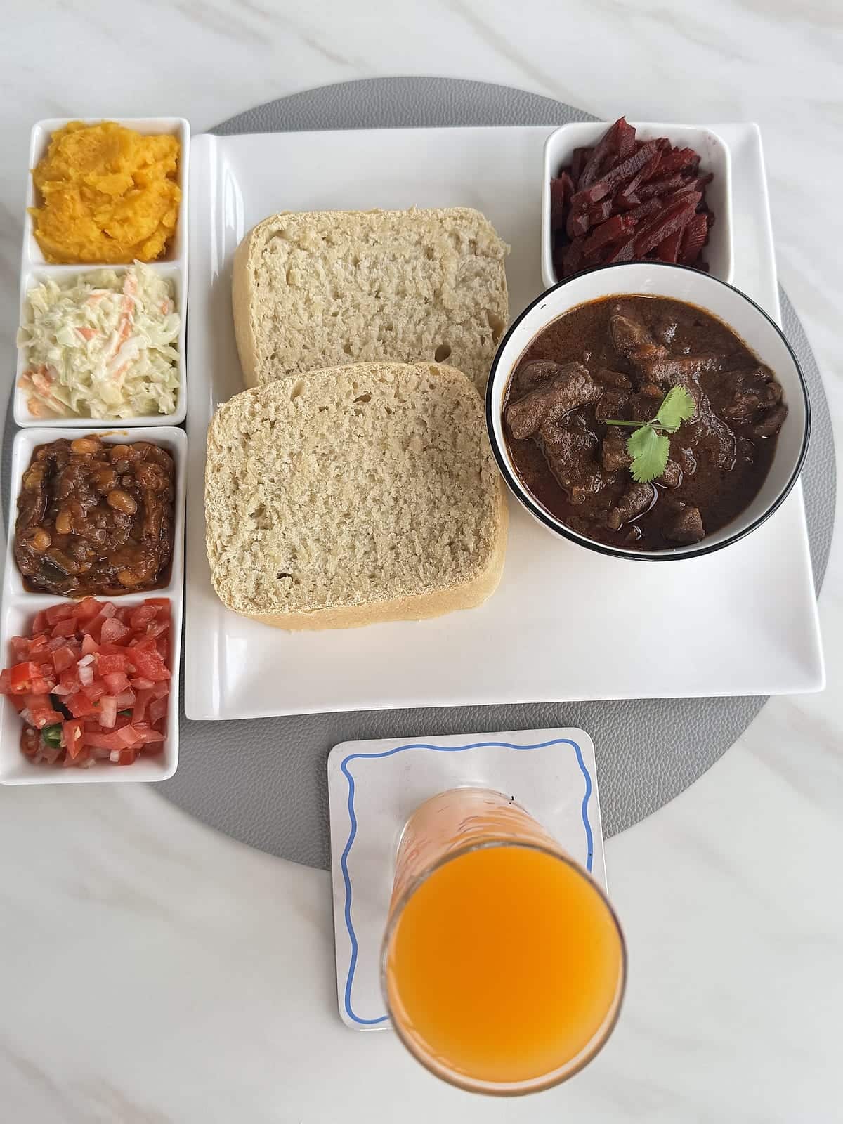 Beef stew served with thick slices of steamed bread, beetroot and fresh sides