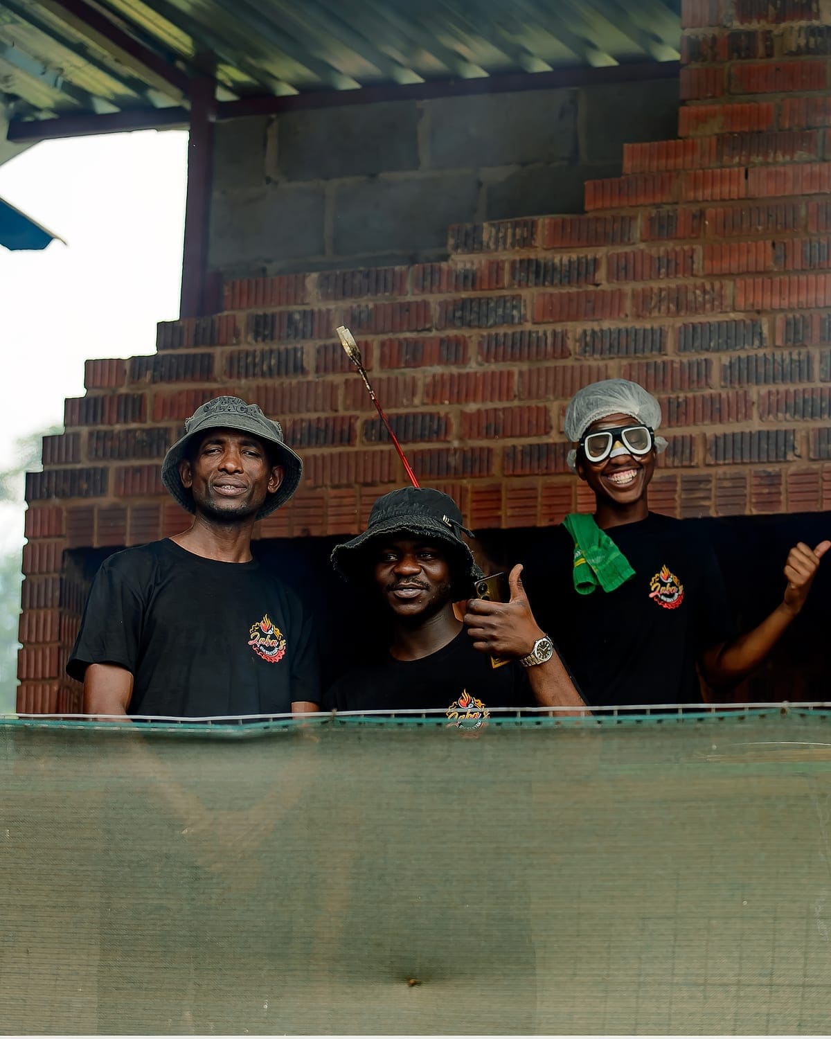 Three Zaba's Shisanyama staff in branded shirts standing at the brick braai, one holding tongs