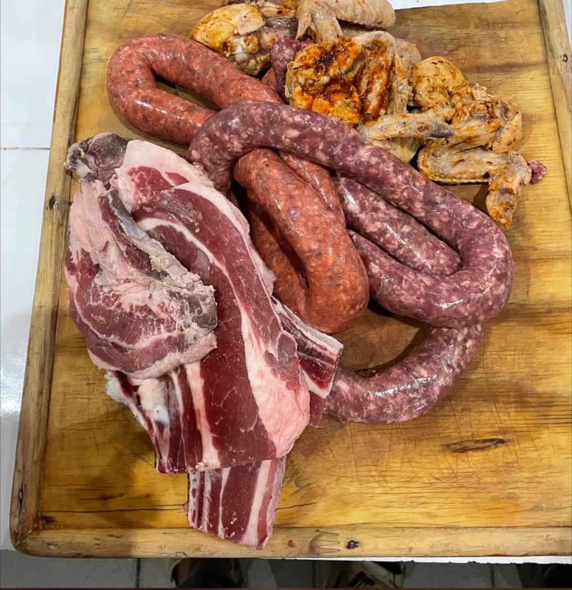 Fresh lamb chops, boerewors coils and marinated chicken laid out on a wooden block, ready for the fire