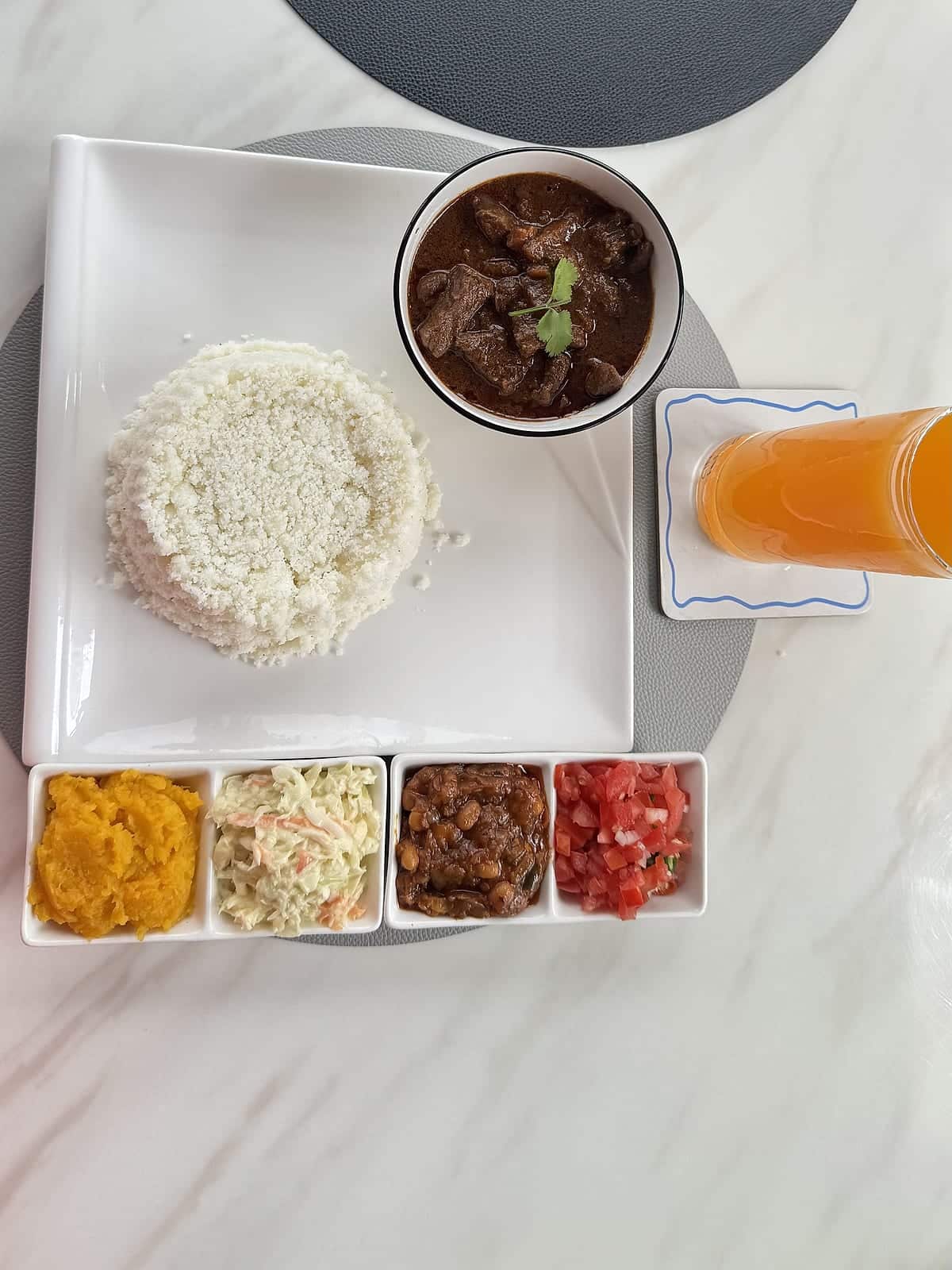 Beef stew with pap, chakalaka, coleslaw, butternut and tomato salsa on a white plate